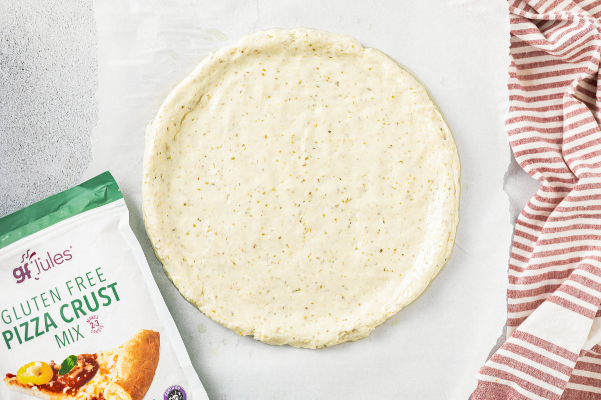 Unbaked gluten-free pizza crust round on parchment, pale and speckled