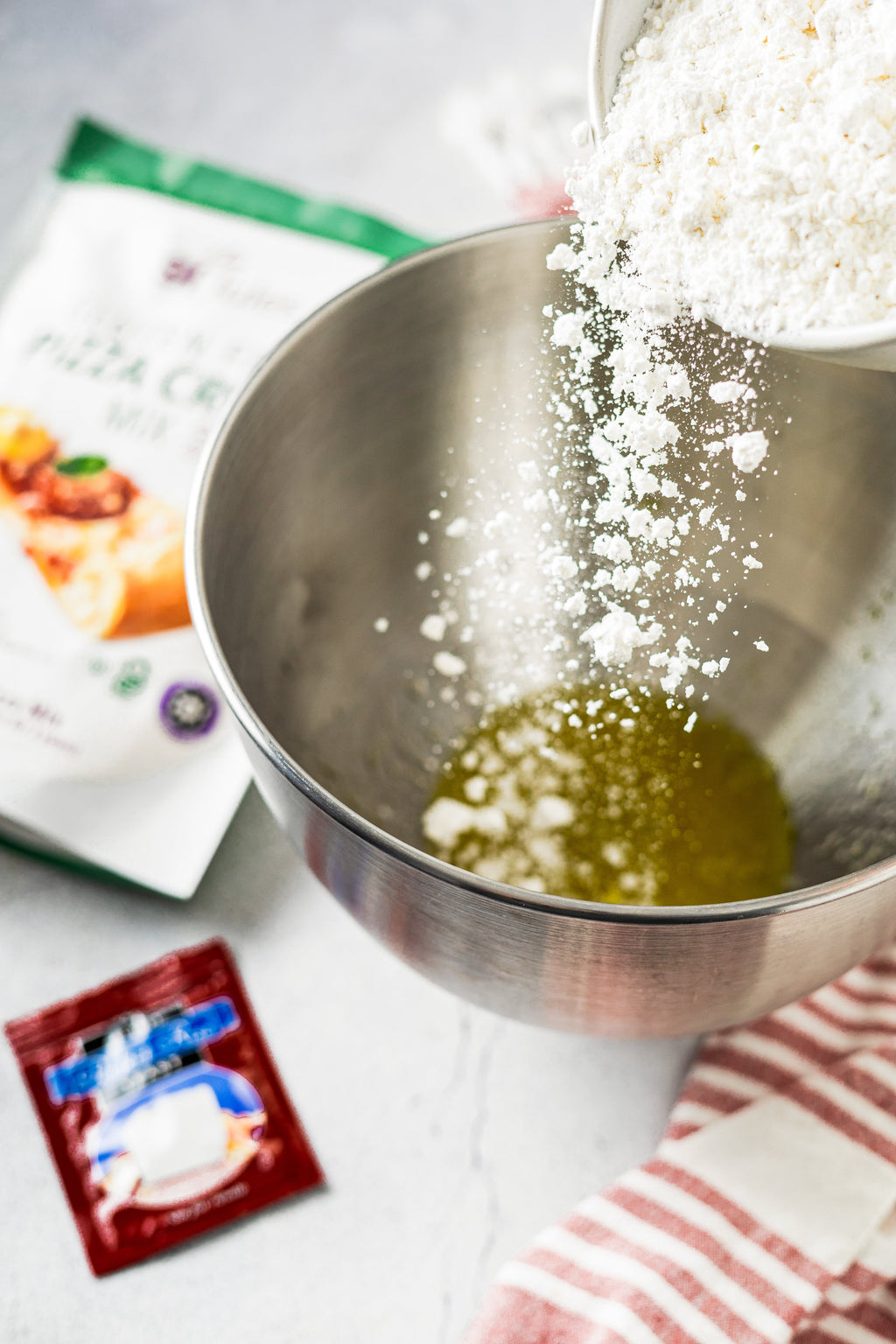 Gluten-free pizza crust mix being poured into a mixing bowl with oil