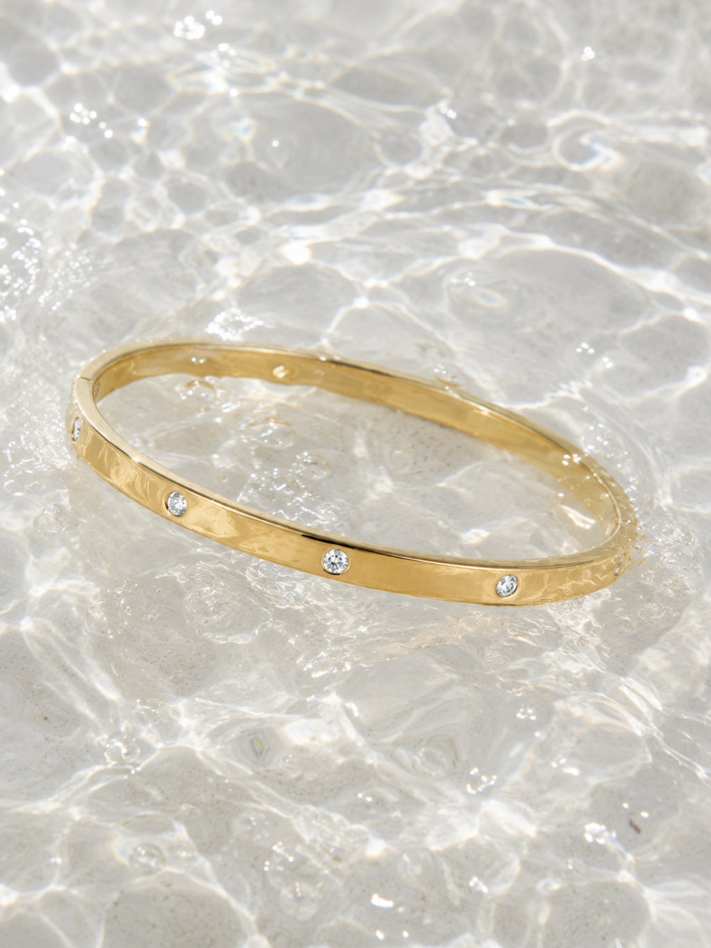 Gold-tone diamond bangle with three round stones across the front, on marble-like texture