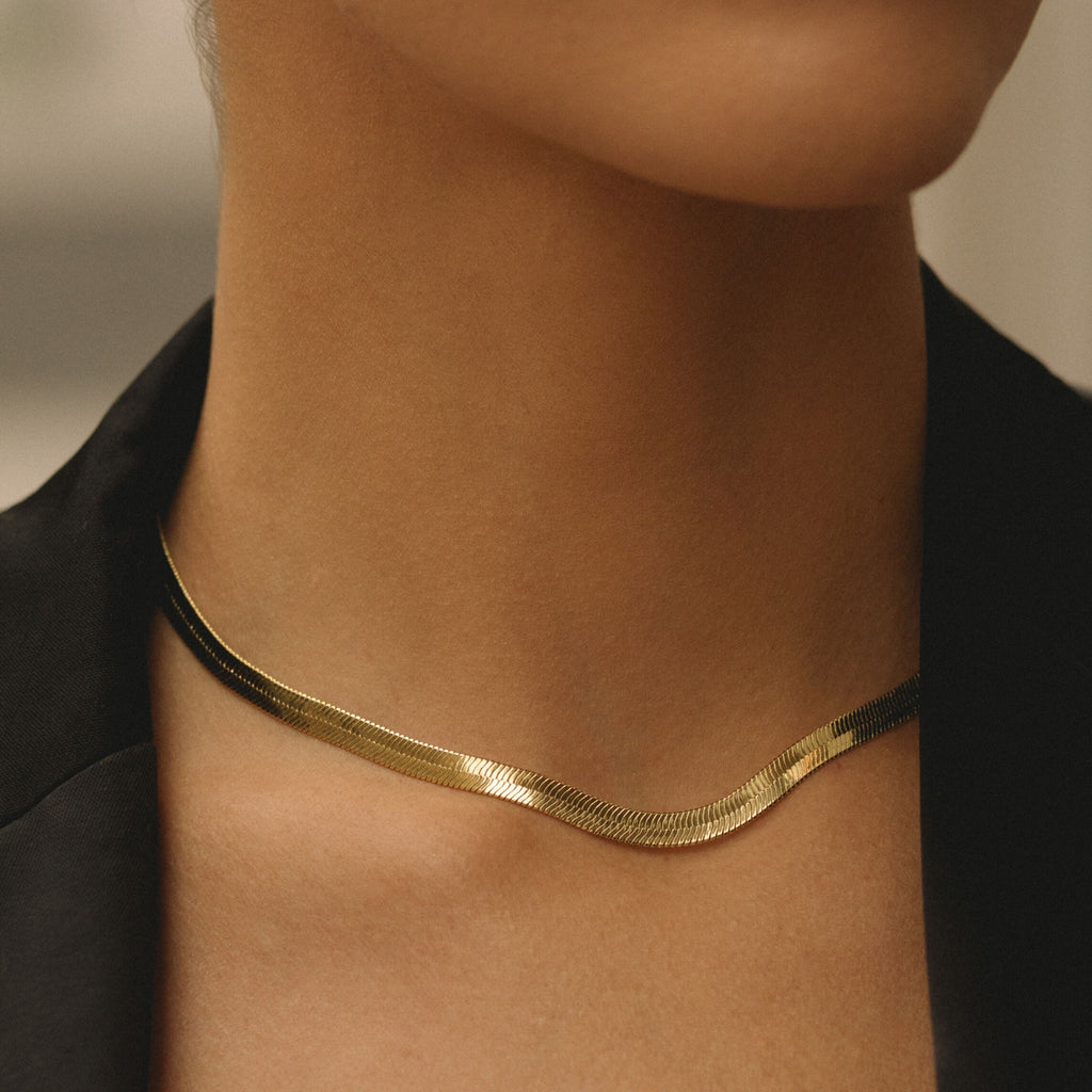 Gold herringbone chain necklace worn at the base of the neck