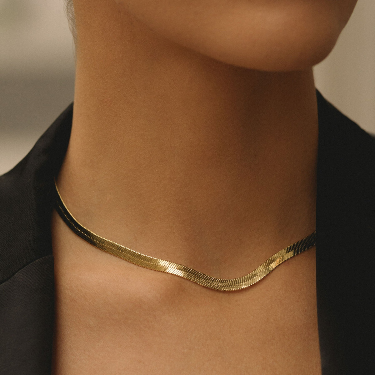 Gold herringbone chain necklace worn at the base of the neck