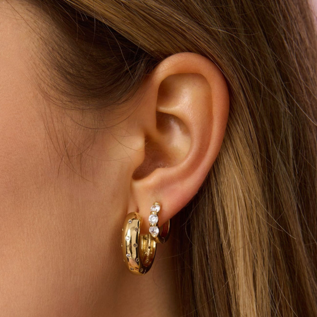 Gold-tone huggie hoop earrings with three clear stones, side view detail