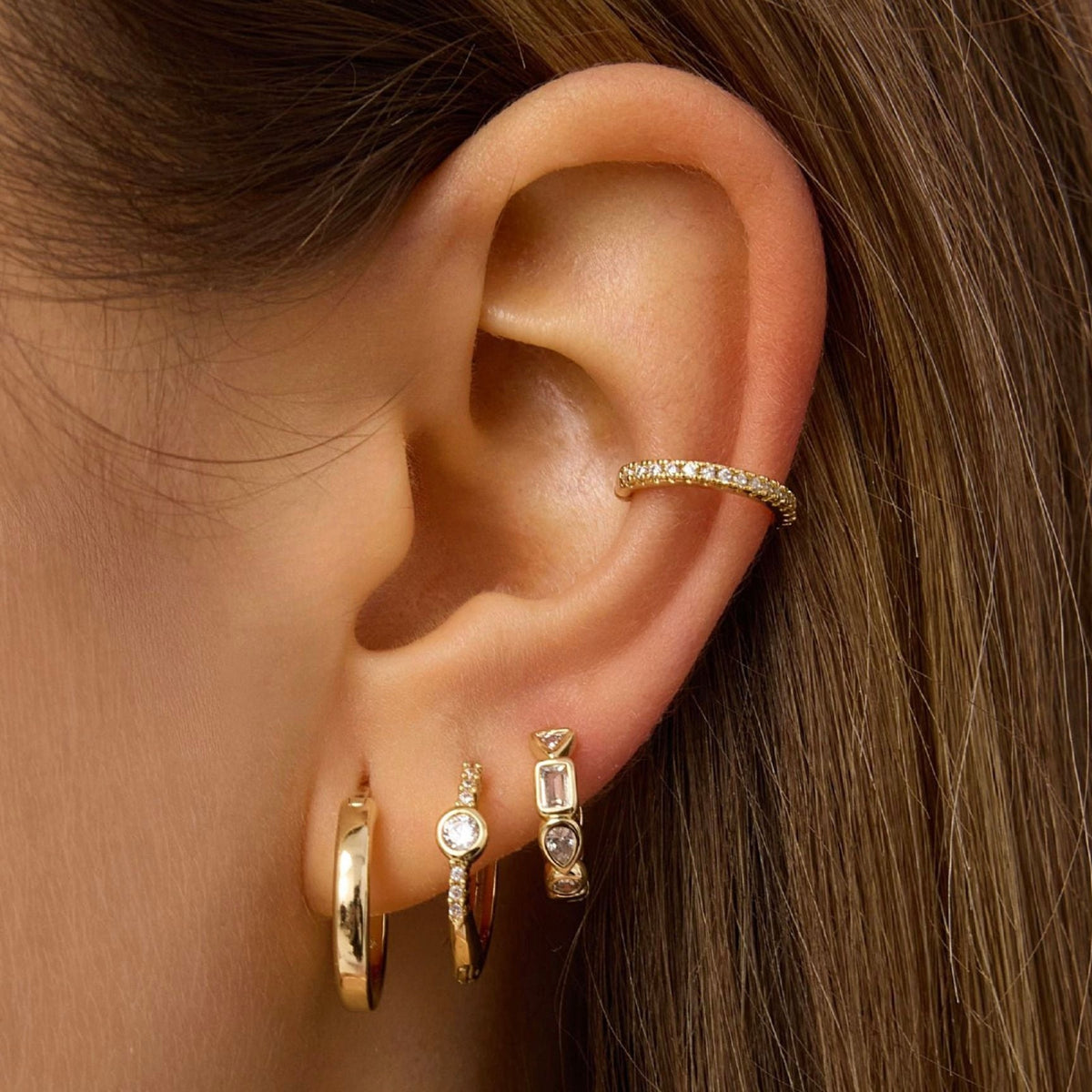 Gold hoop earrings with rectangular clear gemstone accents worn on ear