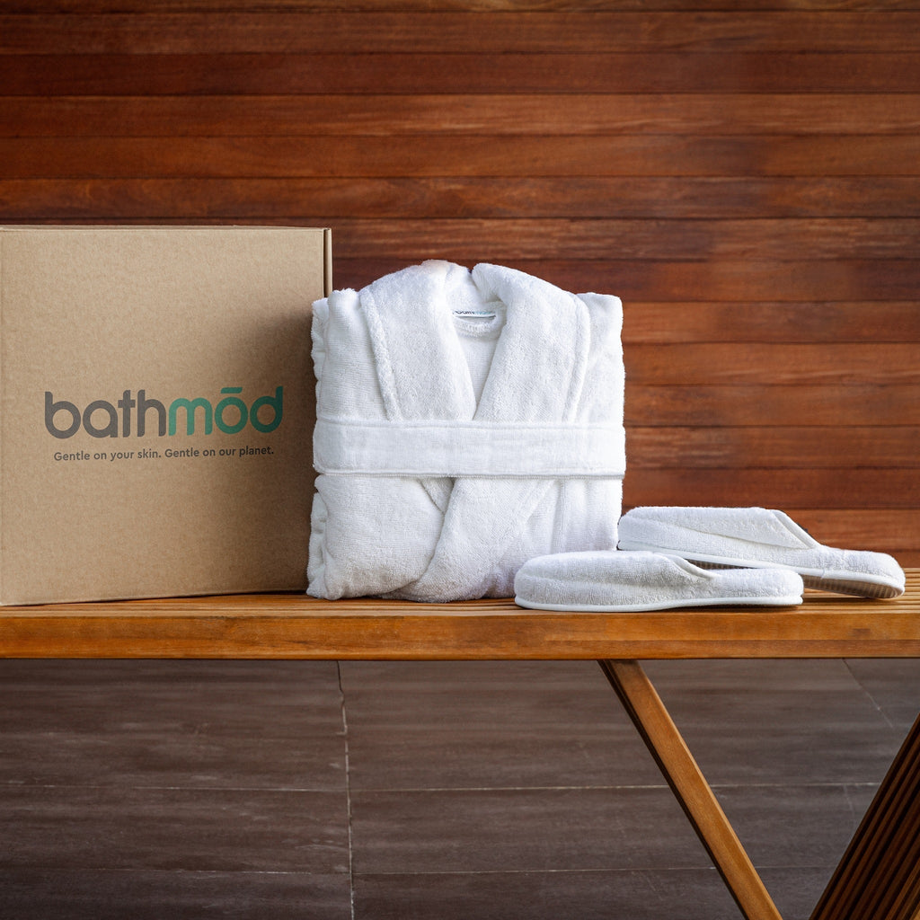 Folded white bathrobe with matching slippers laid on a wooden bench
