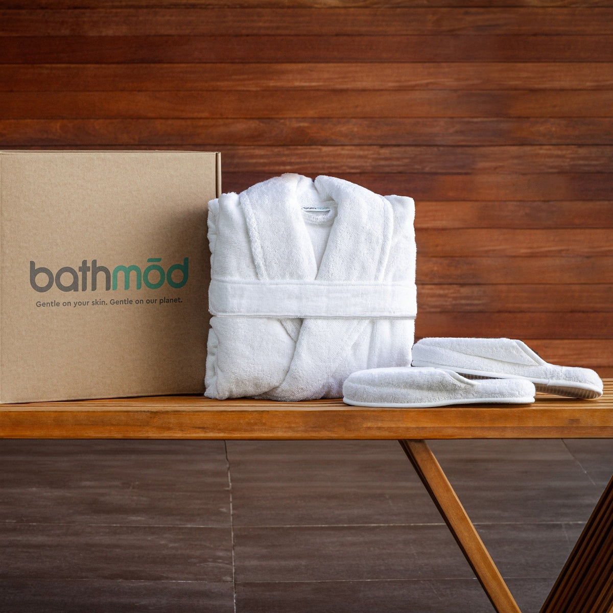 Folded white bathrobe with matching slippers laid on a wooden bench