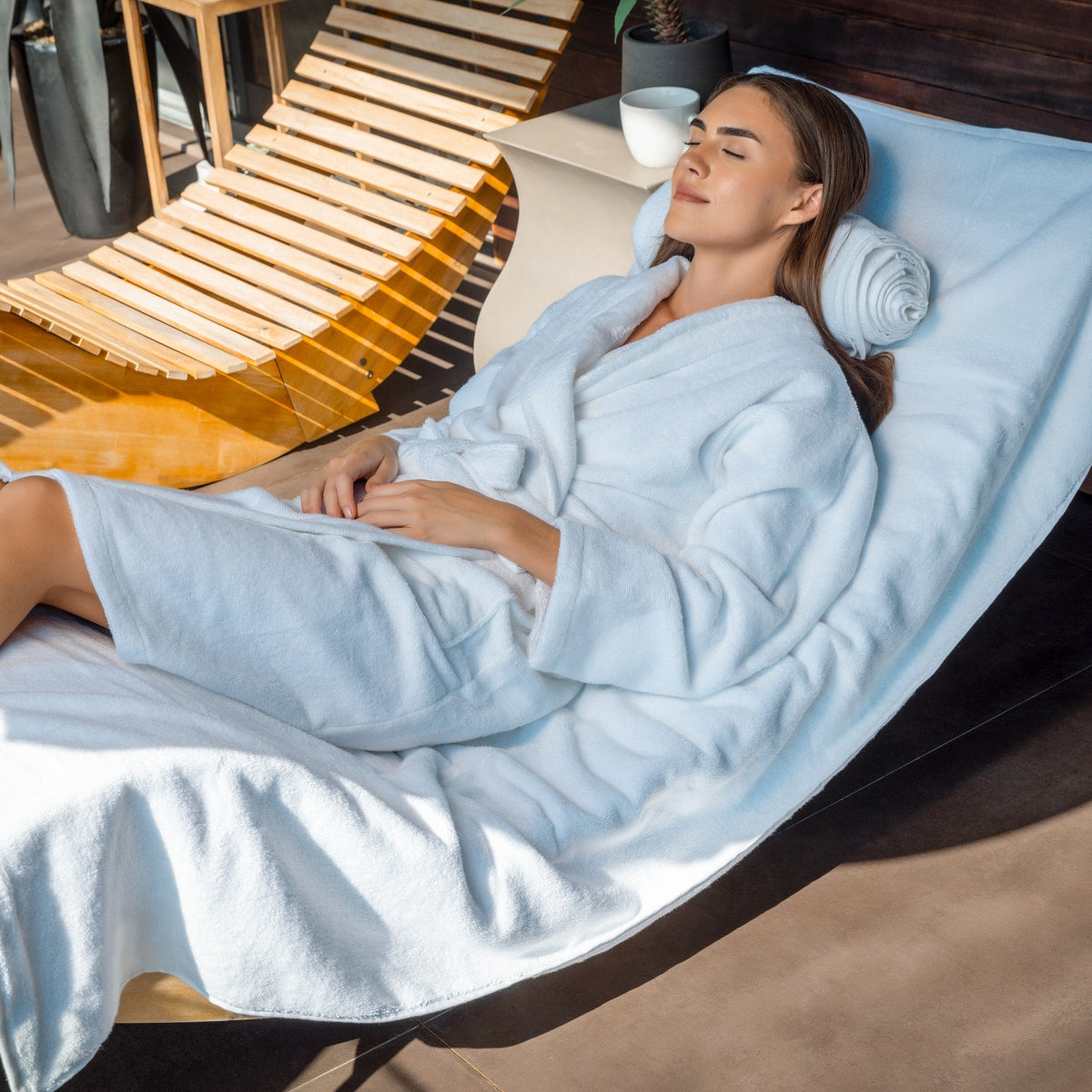 Light blue terry bathrobe laid over lounge cushion, long sleeves and belt tie