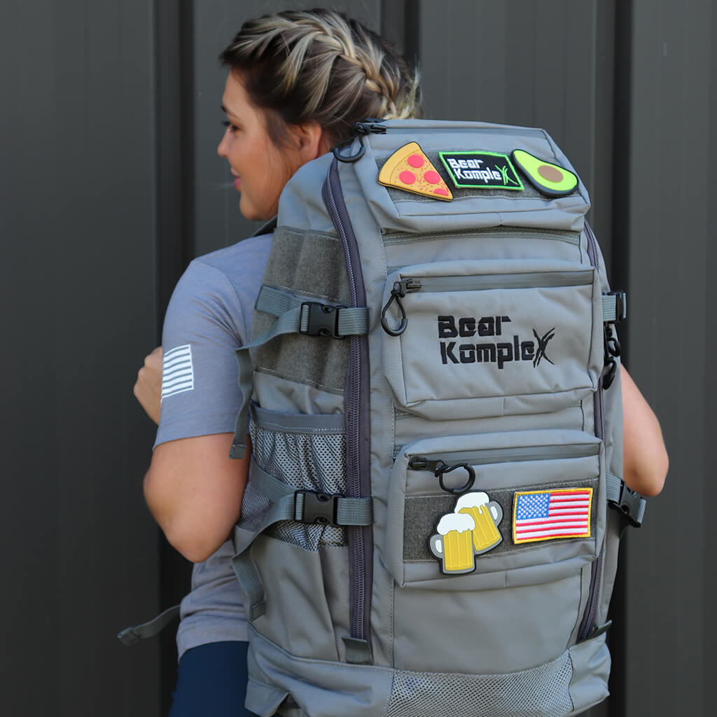 Light gray military backpack with front patches, pockets, and padded back panel