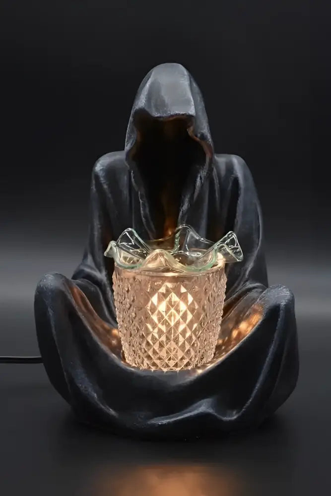 Grim reaper wax and oil warmer with glowing amber oil cup inside a glass holder