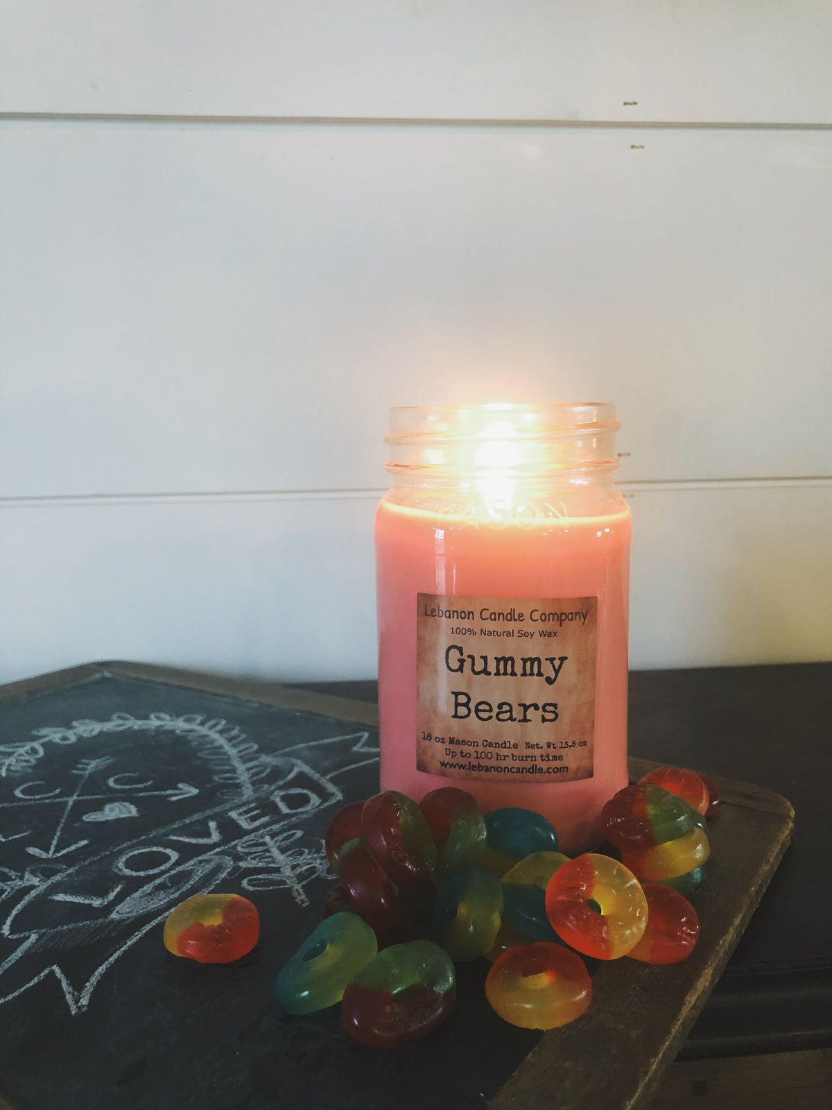 Pink gummy bears scented candle jar with lit flame on a tabletop