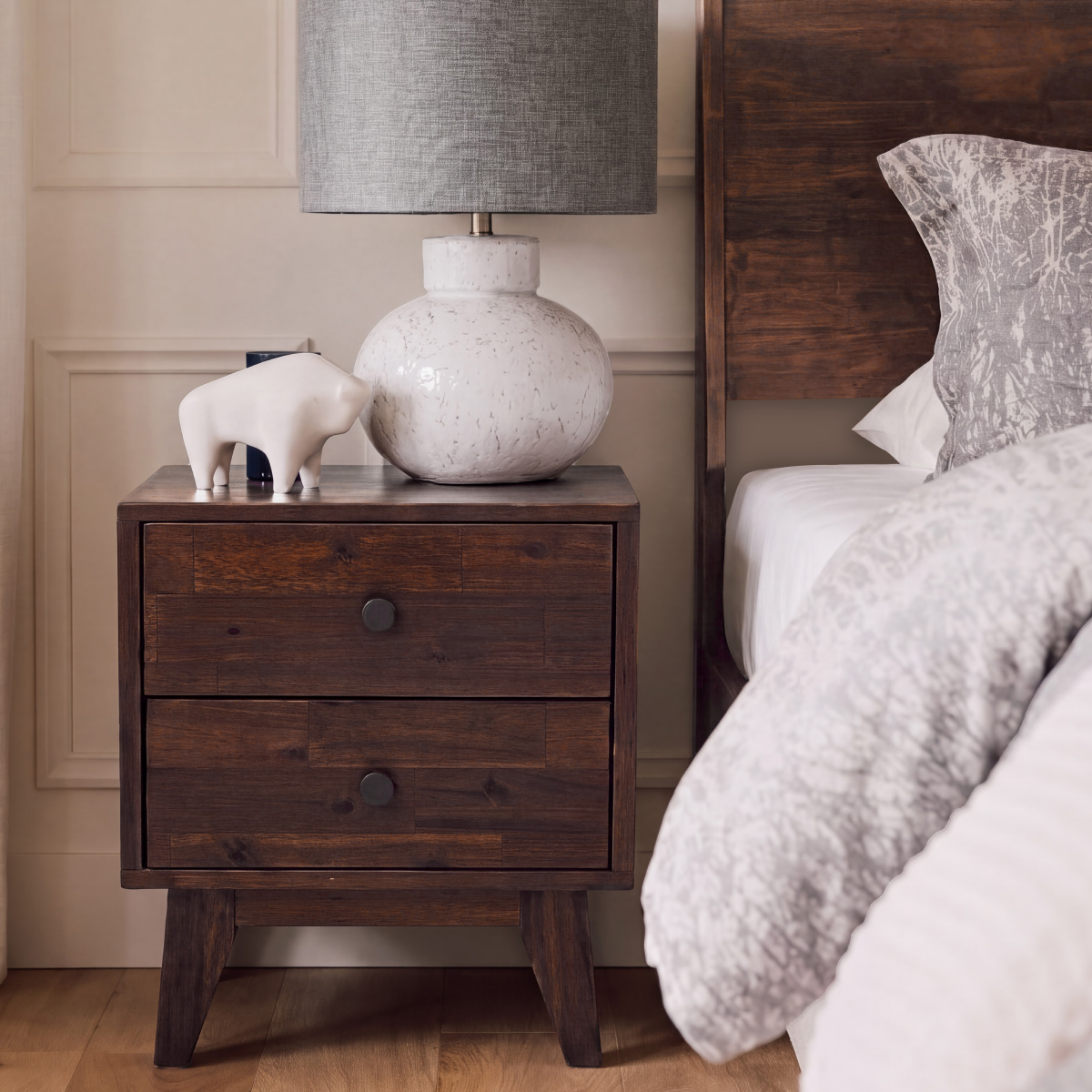Solid wood nightstand with two drawers and round knobs, shown next to a bed