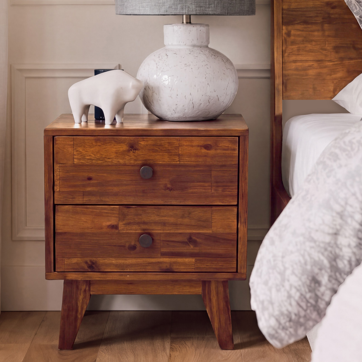 Silvia solid wood nightstand with two drawers and round knobs beside a bed