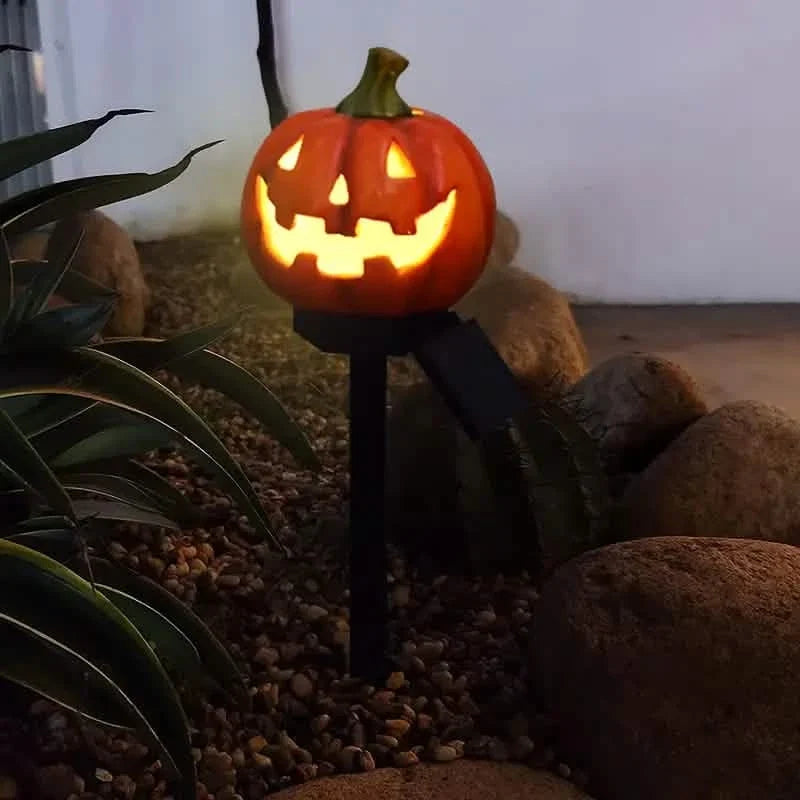 Glowing orange jack-o'-lantern solar stake light with carved grin and green stem