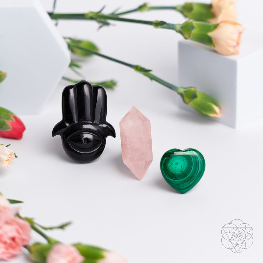 Black hamsa car diffuser with pink rose quartz wand and green heart crystal on white surface