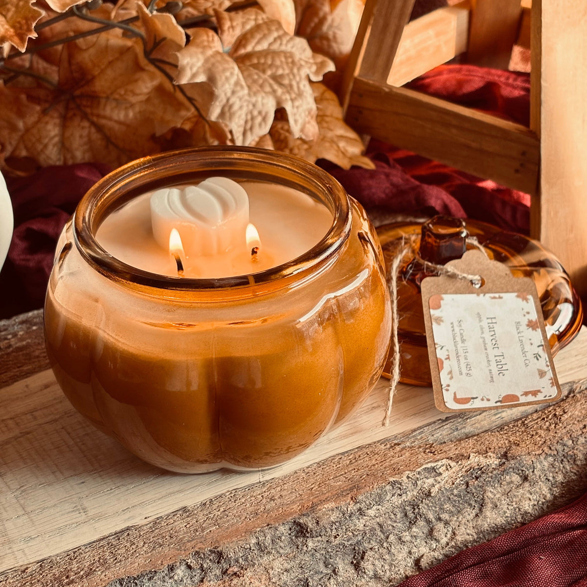 Amber soy candle in round glass jar with lit wicks, with hang tag on side
