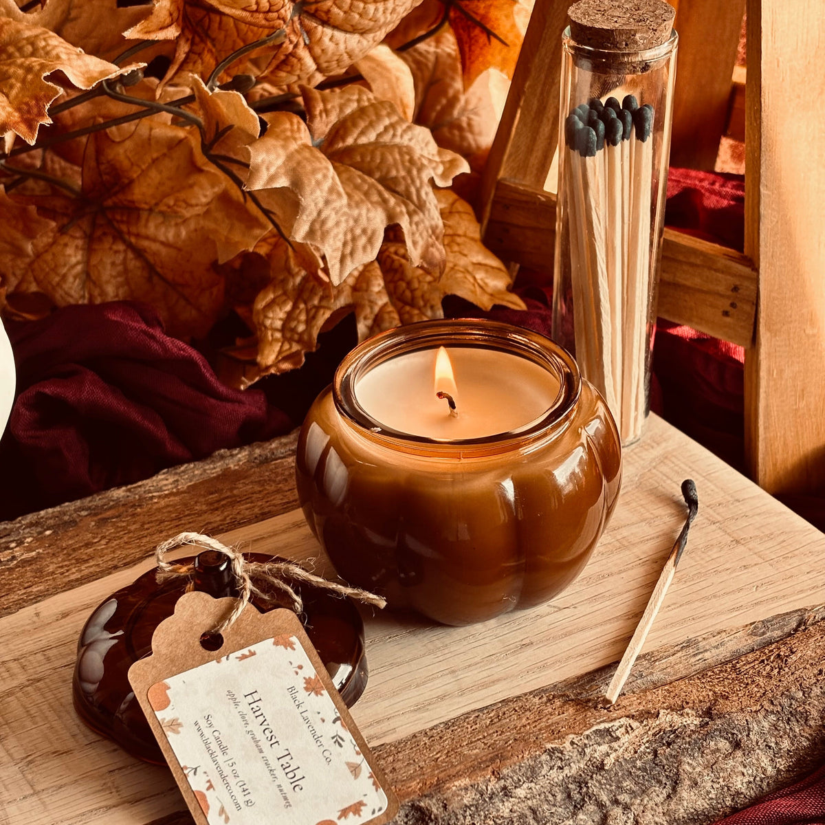 Amber soy candle in glass jar with lit wick, with hang tag on wooden tray