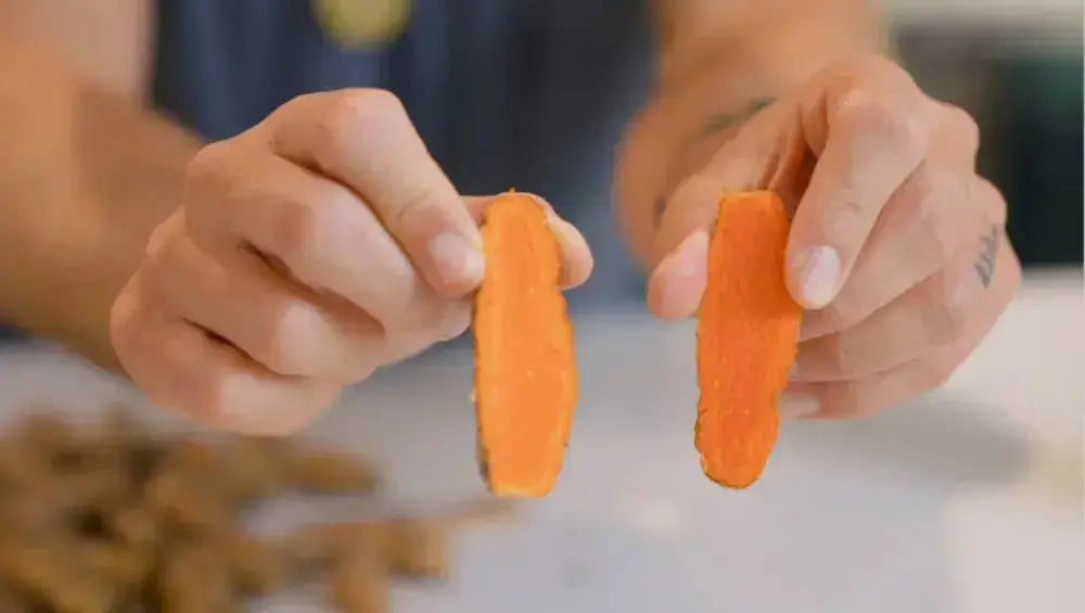 Two hands holding sliced orange turmeric roots over a countertop