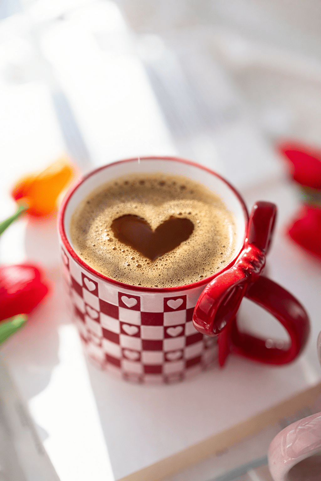 Ceramic mug with red checkered pattern and heart motifs; mug held with both handles