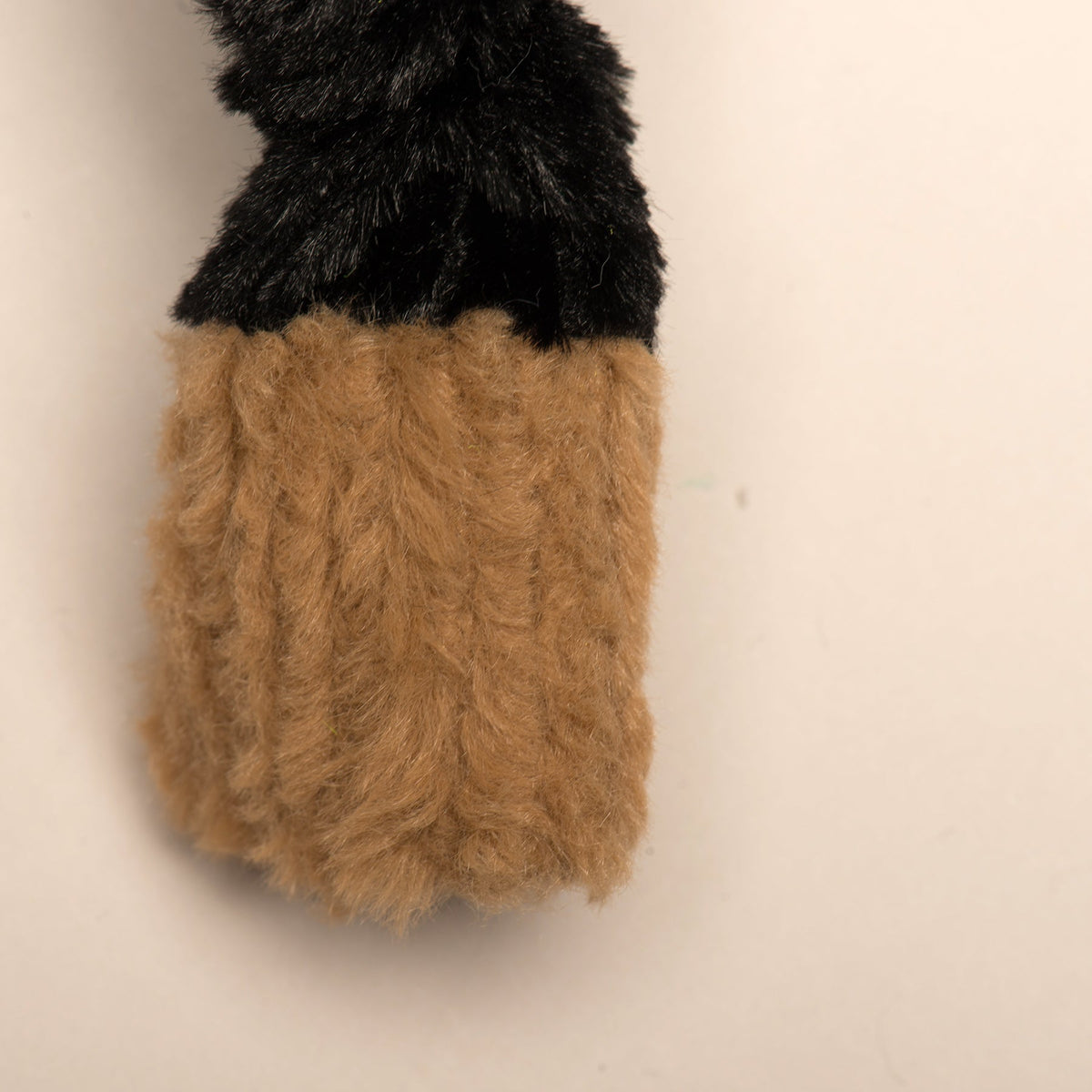 Tan plush paw detail on a black plush dog toy