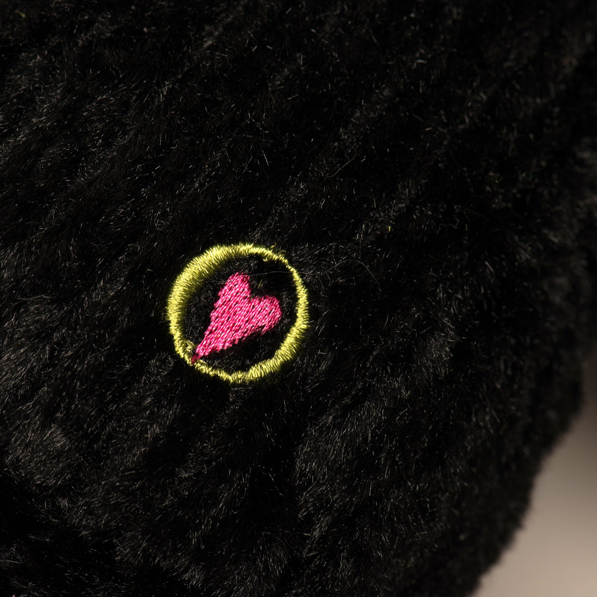 Black plush dog toy with round neon-accent emblem patch on shoulder