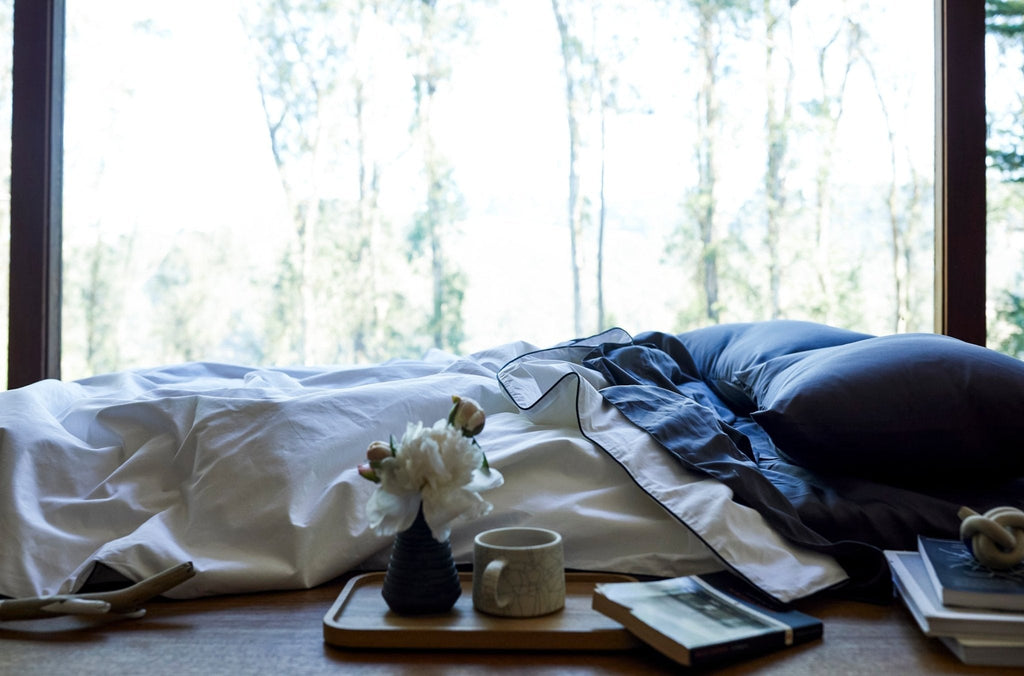Silk-filled duvet set in white with dark piping, draped over a bed with folds