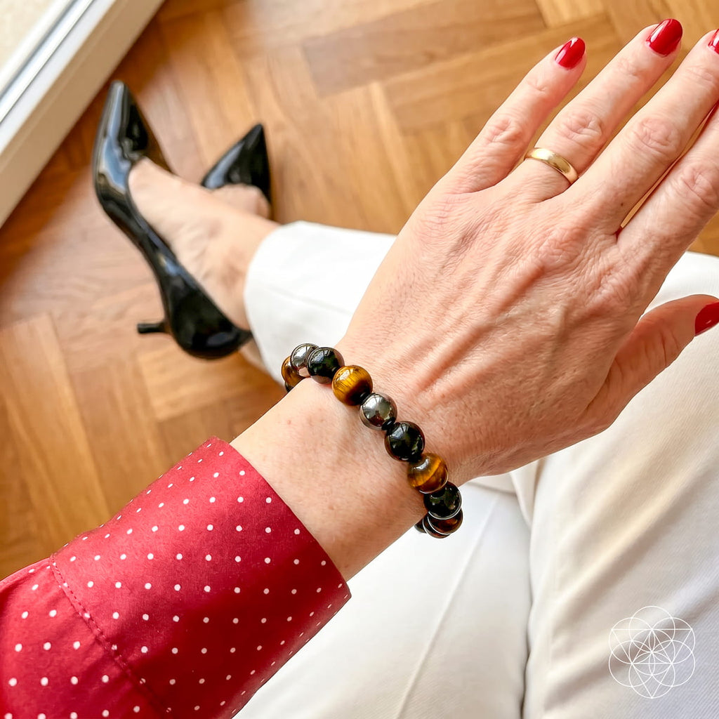 Beaded bracelet on wrist: glossy black stones with warm tiger-eye beads and metallic spacers.