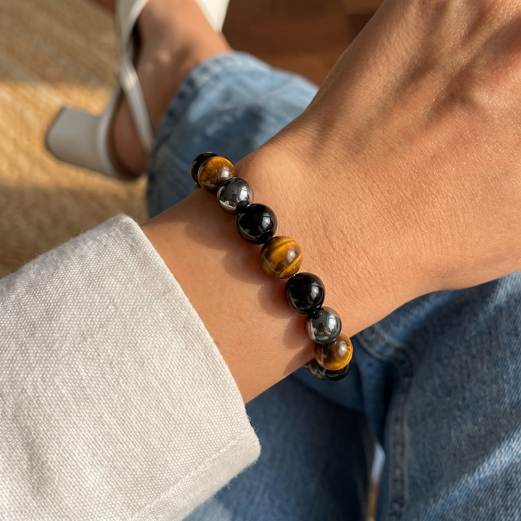 Close-up beaded stretch bracelet with glossy black stones and brown tiger-eye bead accents.