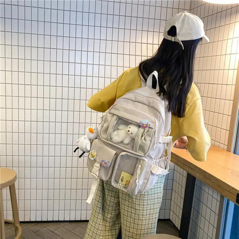 Light cream nylon backpack with front pouch, zipper pockets, and plush duck charm