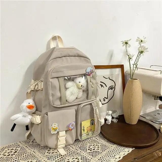 Beige nylon backpack with front compartments, cartoon patches, plush bear and duck charm