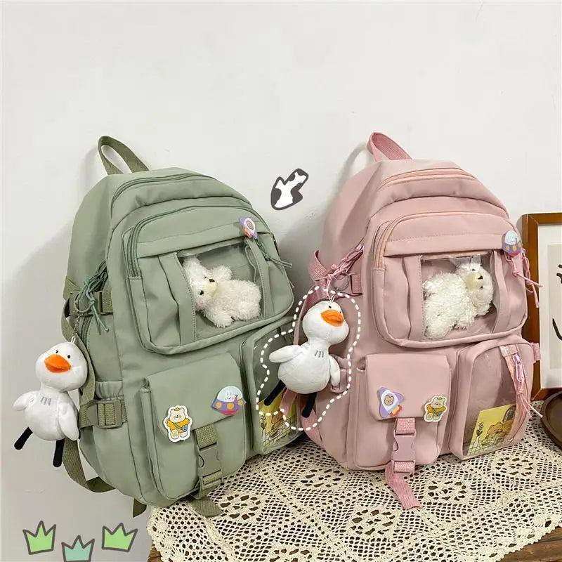 Pair of nylon backpacks: green and pink, each with front pockets and plush charm