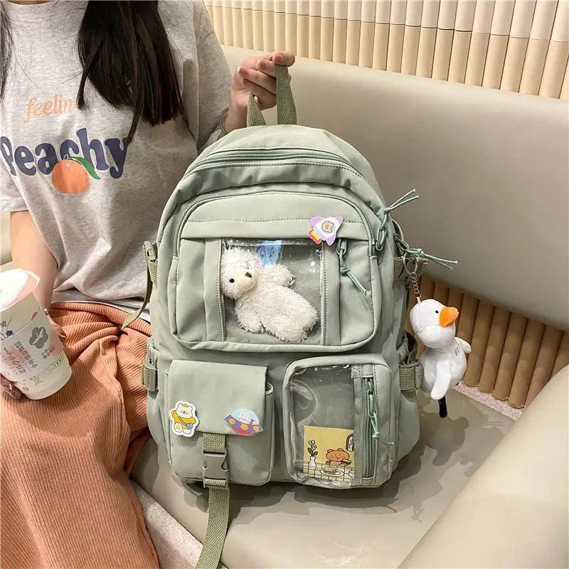 Sage green nylon backpack with front pockets, cartoon patches, plush bear and duck charm