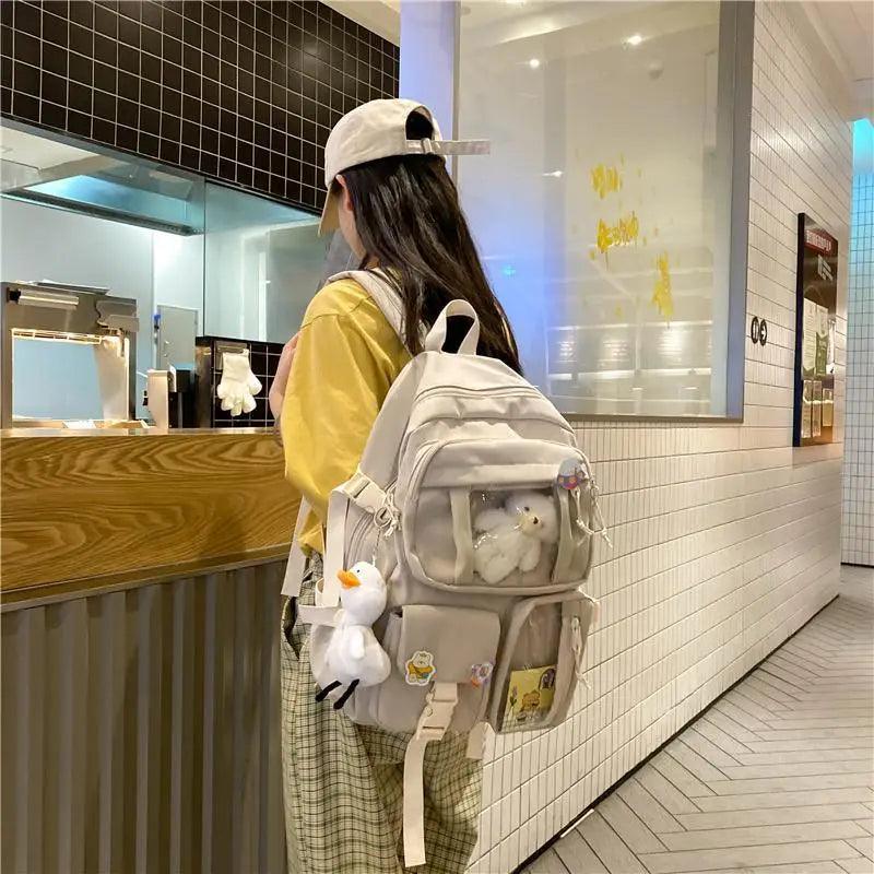Beige mini backpack with plush bear, side strap, and front zipper pocket details