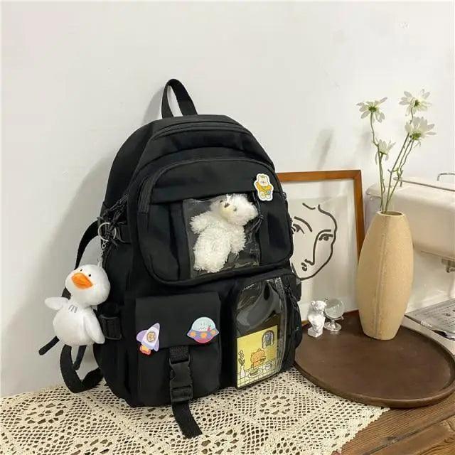 Black nylon backpack with multiple front pockets, cartoon badges, plush bear and bag charm