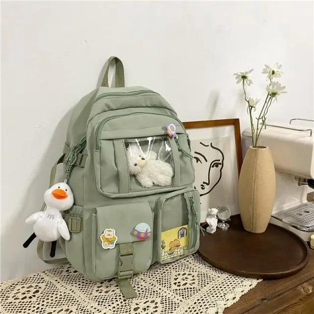 Olive green nylon backpack with clear front pocket, cartoon patches, plush bear and duck charm