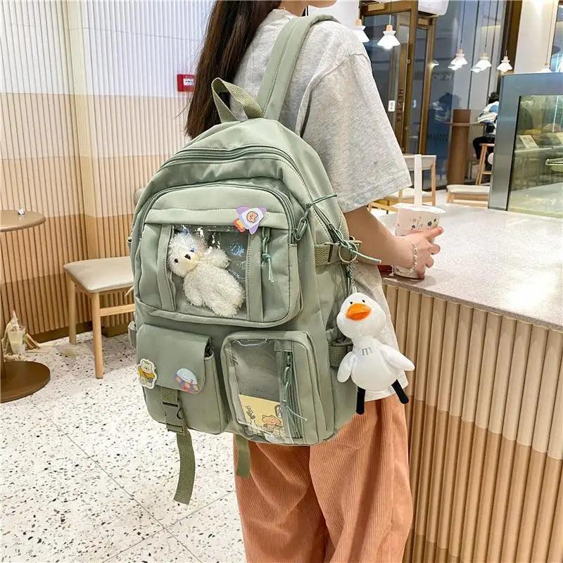 Sage green nylon backpack with zip compartments, front badge patches, plush bear and duck