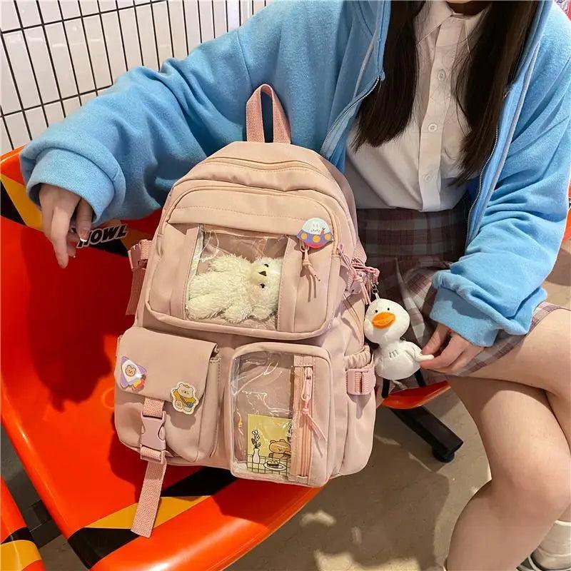 Light beige/pink nylon backpack with front pockets, plush bear, duck charm and shoulder straps
