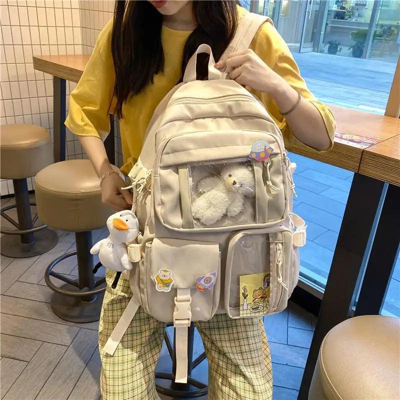 Cream nylon backpack with layered front pockets and plush duck keychain