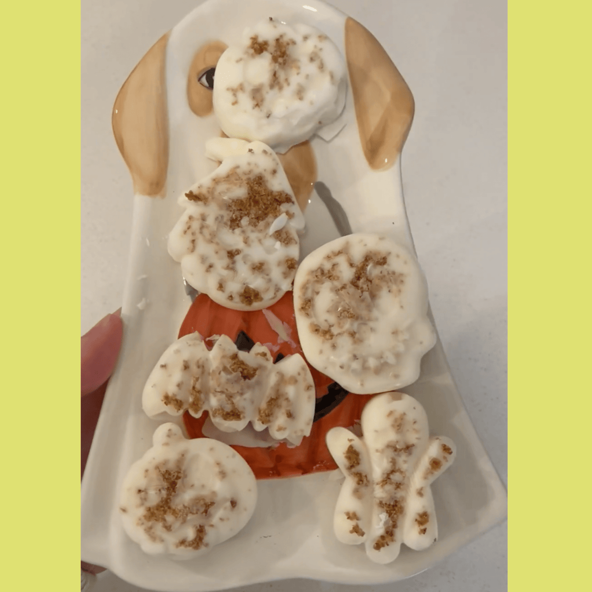Paw-shaped dog treats on a white platter with dark speckled tops