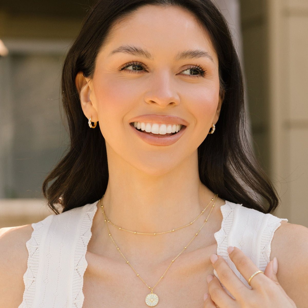 Gold-tone huggie hoop earrings with three clear stones, model face close-up