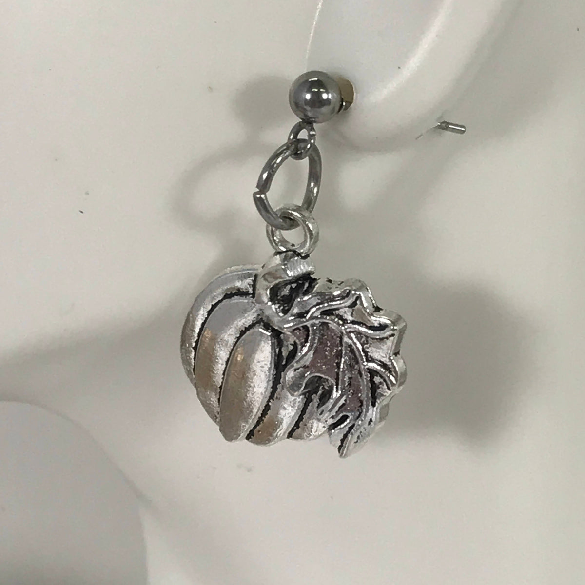 Silver-tone pumpkin dangle earring close-up with ball post and leaf stem charm.