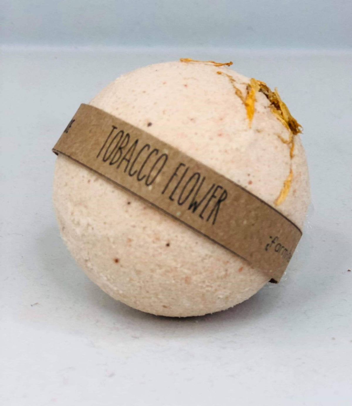 Round bath bomb with brown paper label reading tobacco flower