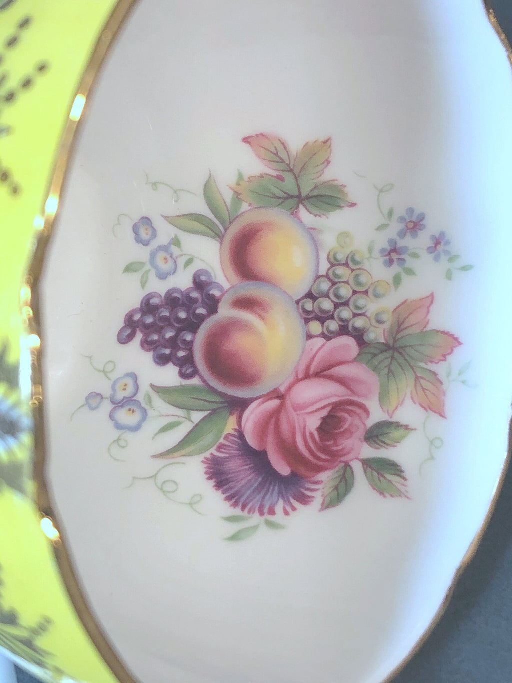 Tight close-up of pink roses, grapes, and fruit floral design on white porcelain