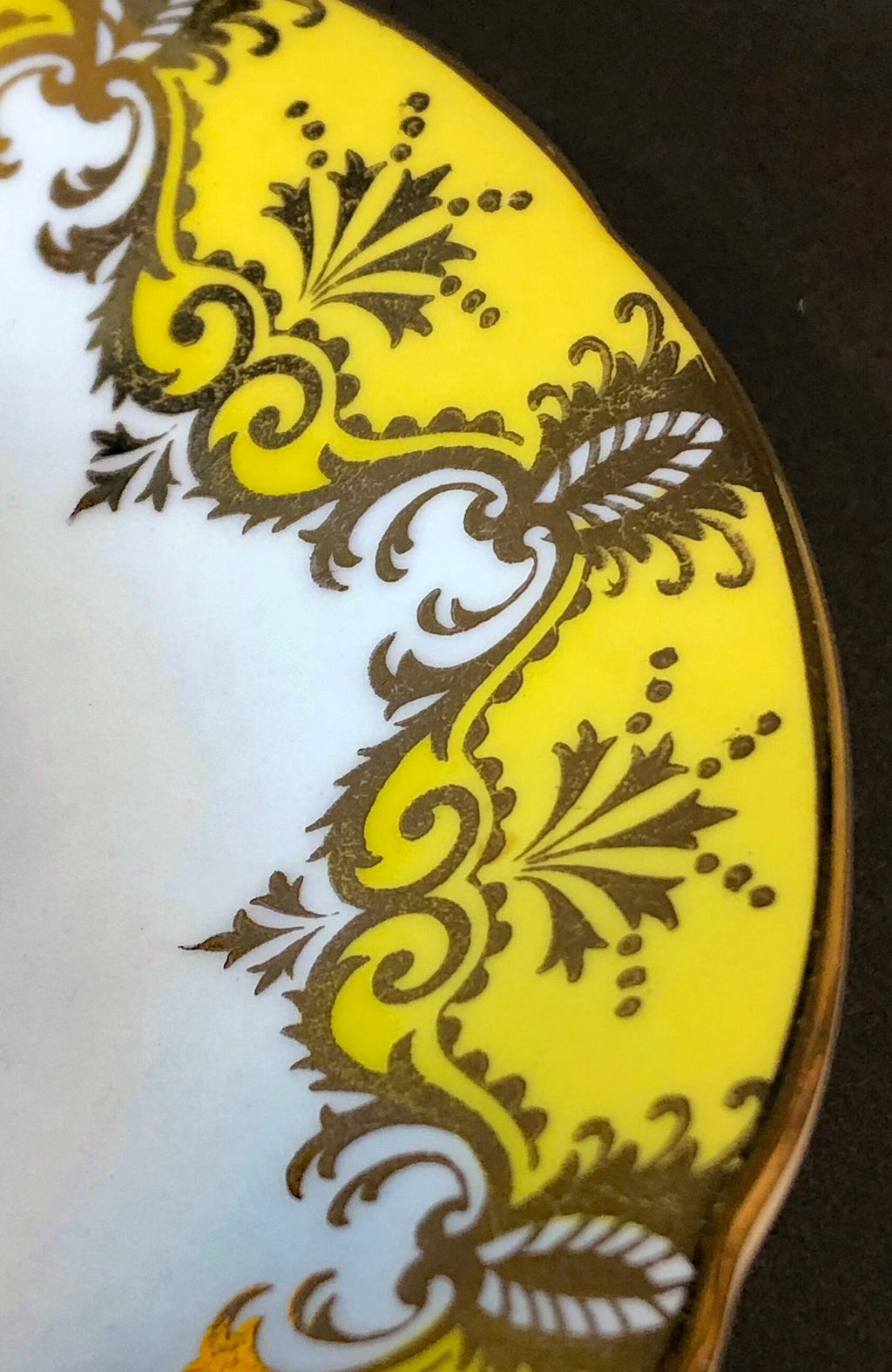 Side view of yellow porcelain saucer with ornate gold scrollwork and floral accents
