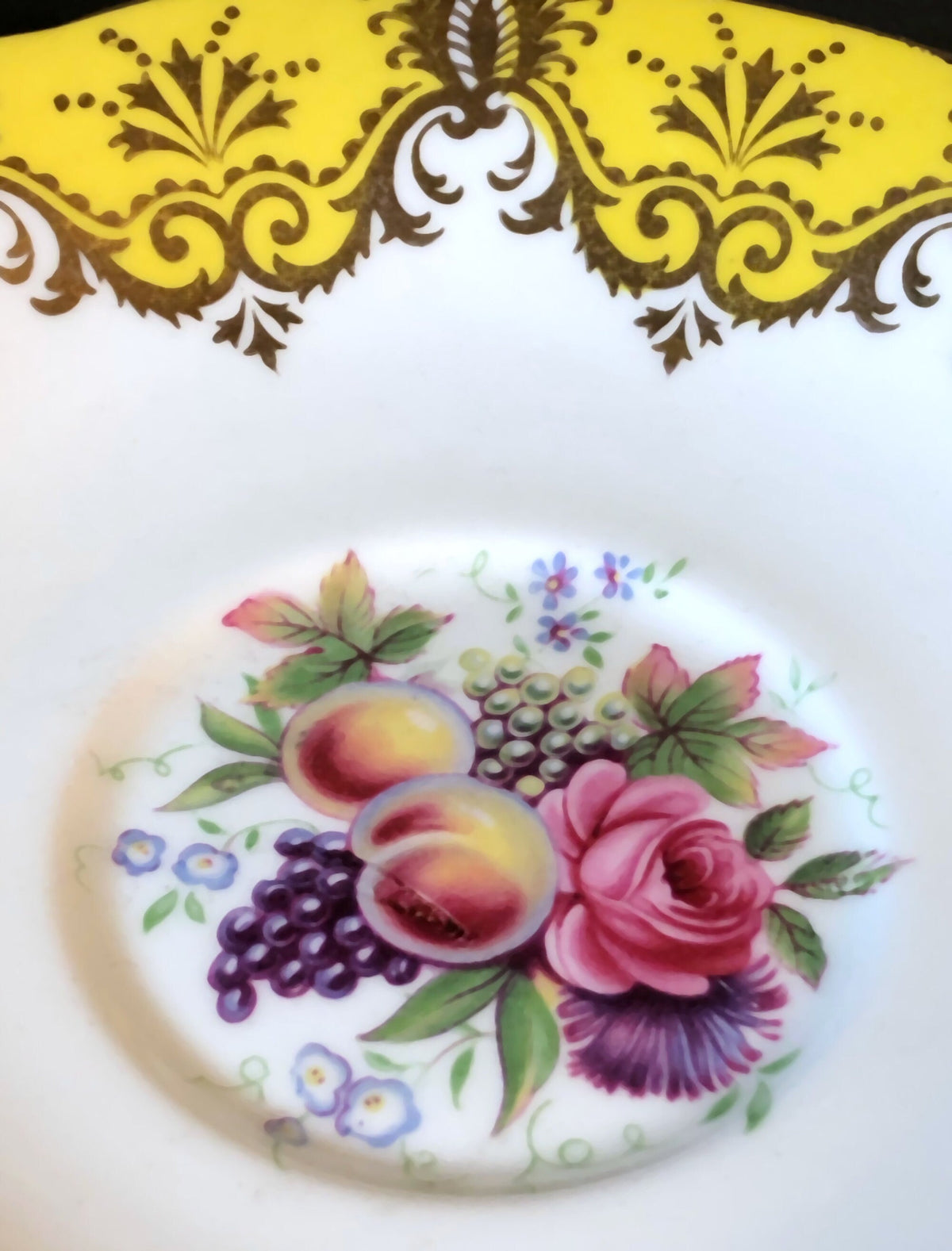 Close-up of floral fruit medallion on white porcelain saucer rim in yellow and gold