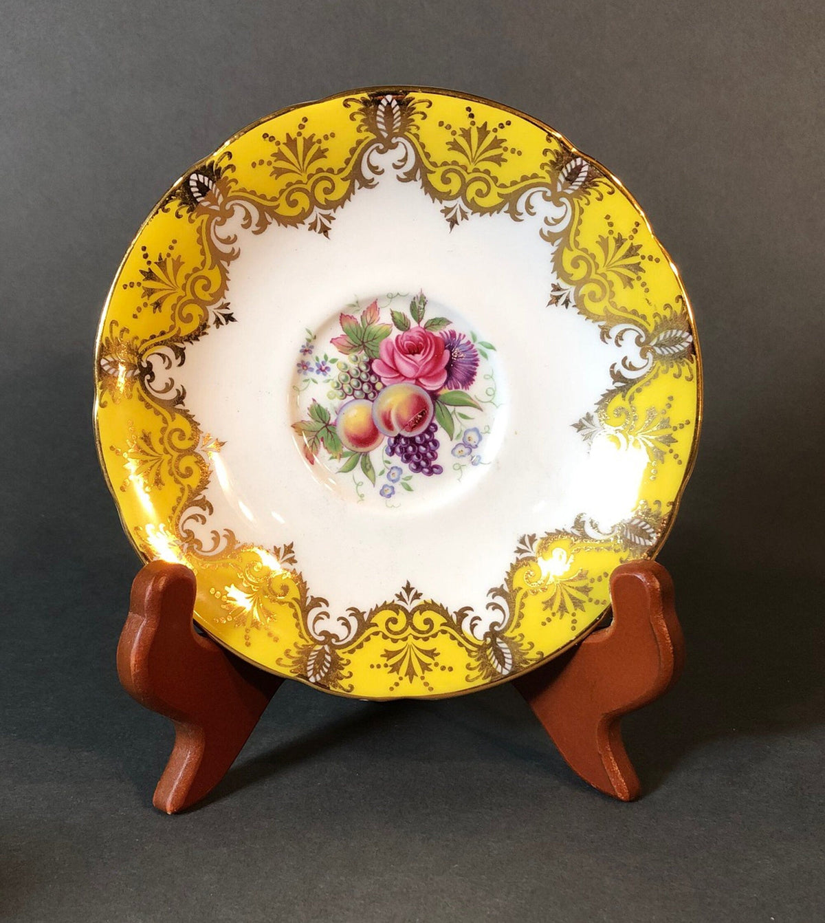 Decorative yellow and gold tea saucer with pink rose, grapes, and fruit medallion