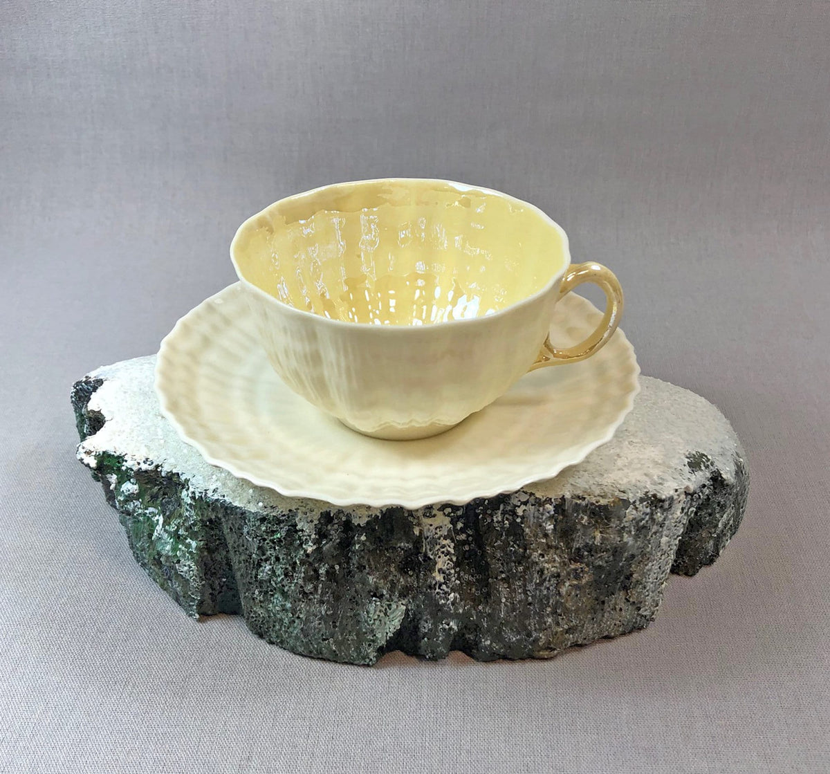Porcelain teacup and saucer set with pale yellow glaze, scalloped rim detail.
