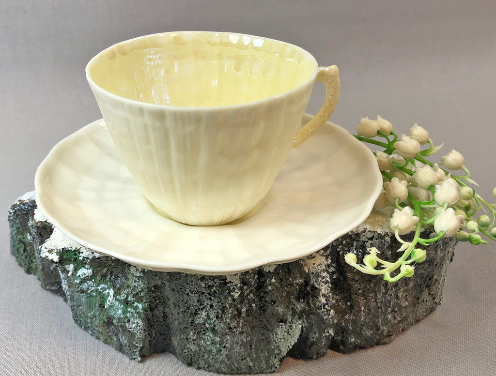Pale yellow porcelain teacup and saucer with seashell pattern, rounded handle.