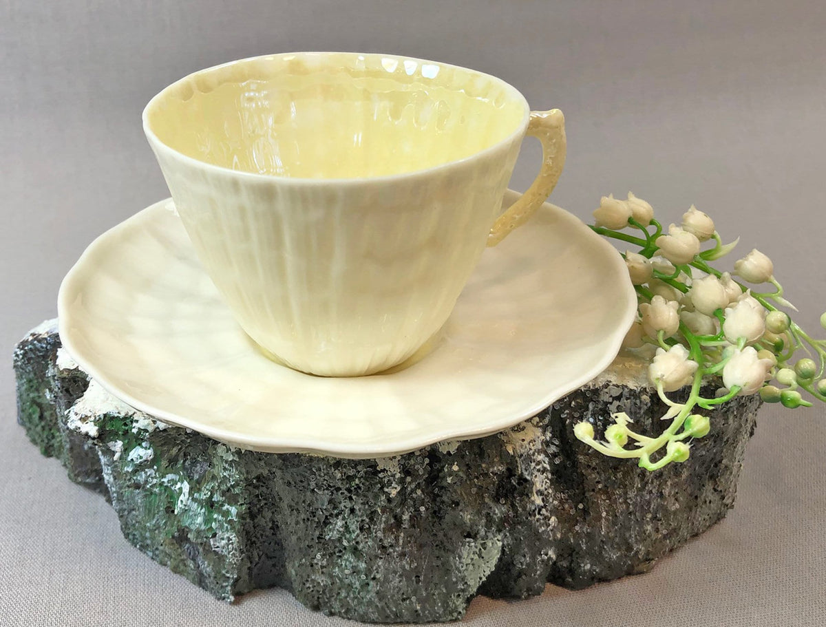 Pale yellow porcelain teacup and saucer with seashell pattern, rounded handle.