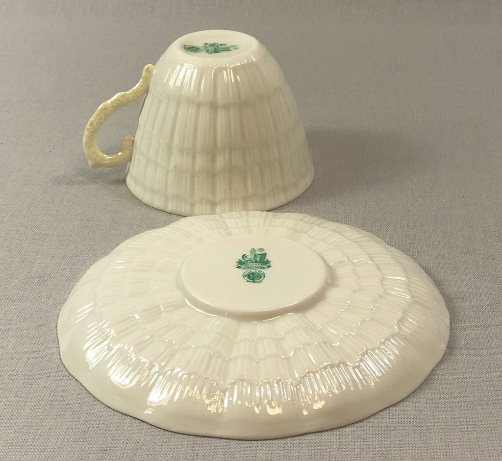 Porcelain teacup with handle and matching saucer, green crest detail.