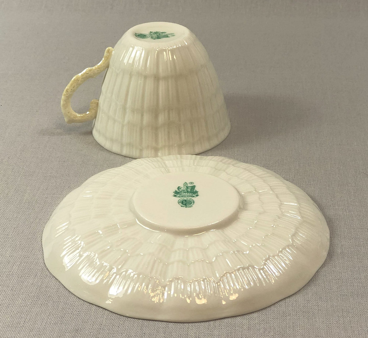 Porcelain teacup with handle and matching saucer, green crest detail.