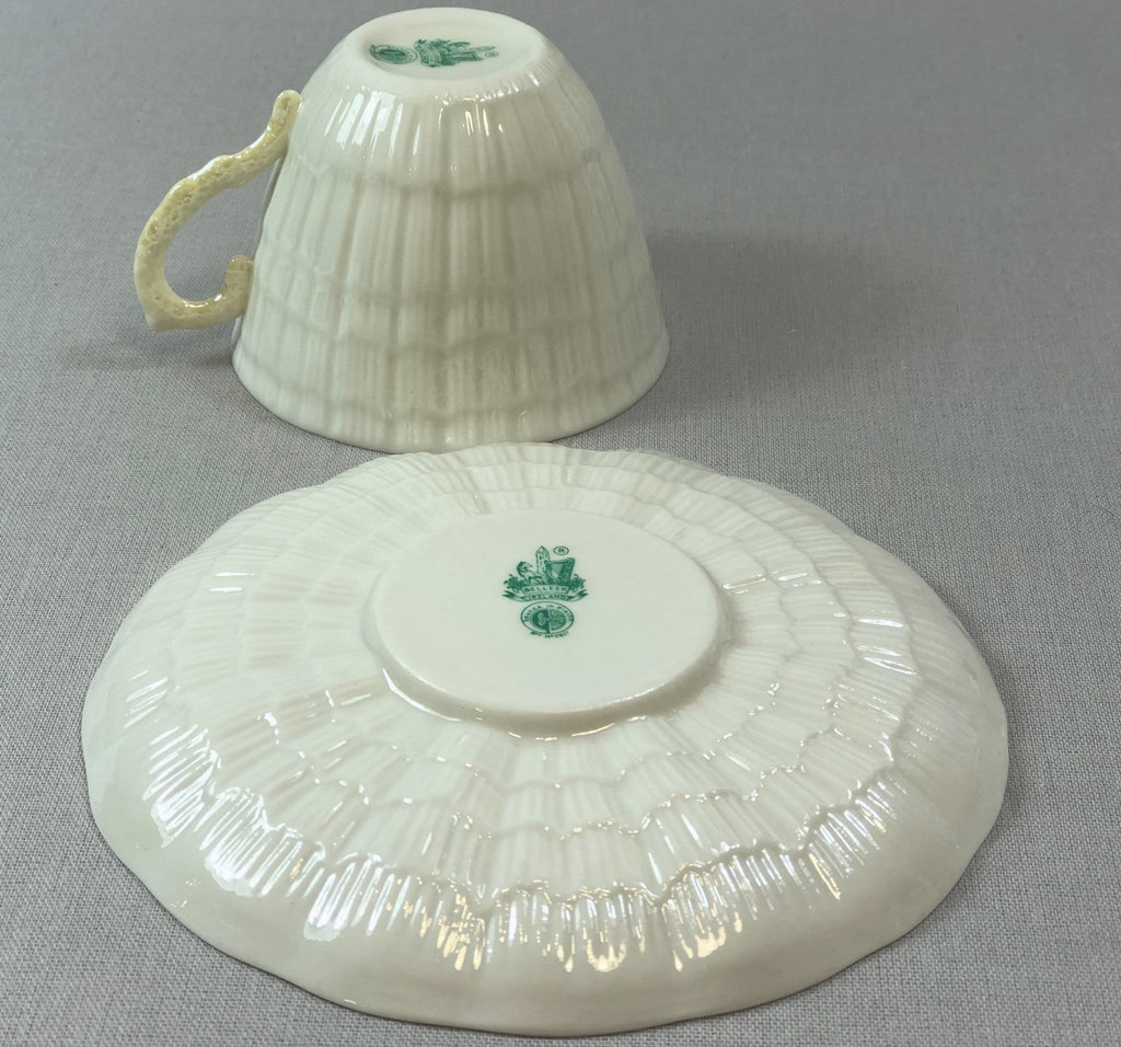 White porcelain teacup and saucer with green emblem, textured ridges.